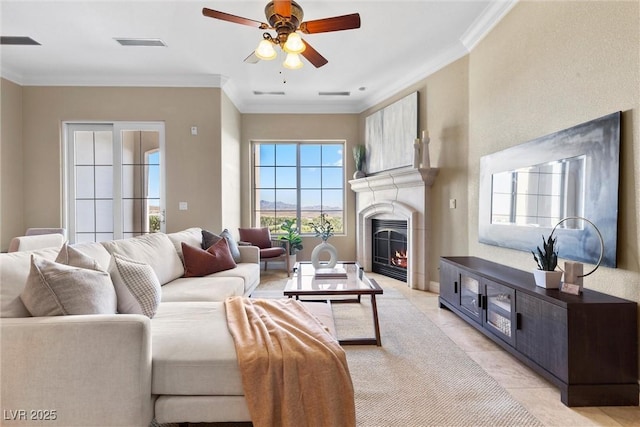 living room with ornamental molding, a lit fireplace, a ceiling fan, and visible vents