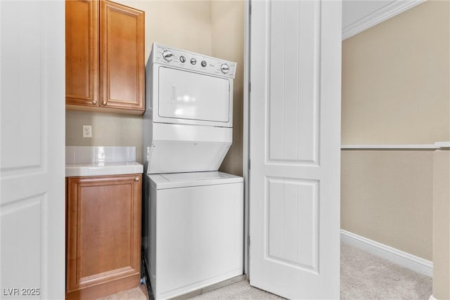 clothes washing area with cabinet space, crown molding, light carpet, baseboards, and stacked washer / dryer