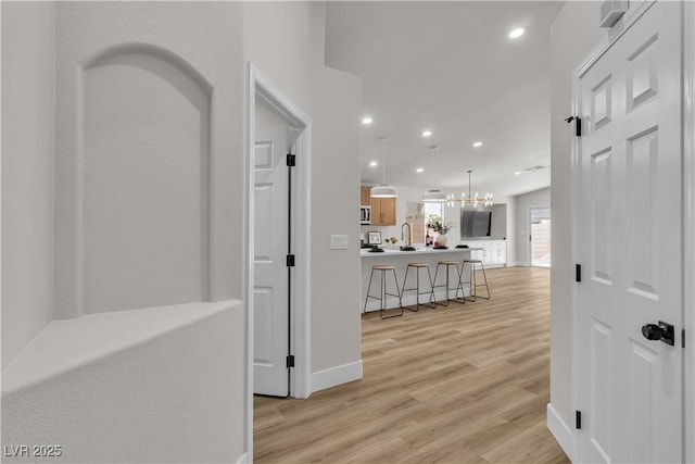 corridor with a sink, light wood-style floors, a chandelier, recessed lighting, and baseboards
