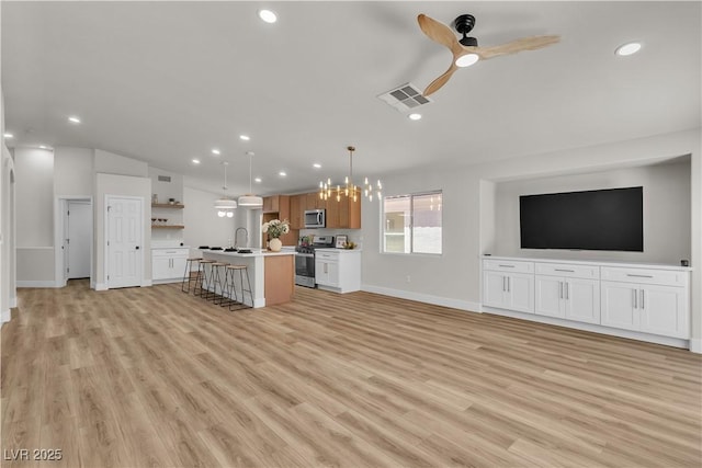 unfurnished living room with recessed lighting, baseboards, light wood-style flooring, and ceiling fan with notable chandelier