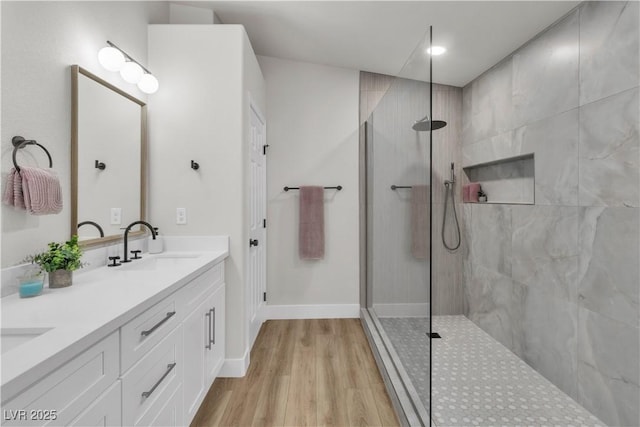 bathroom featuring double vanity, a walk in shower, a sink, and wood finished floors