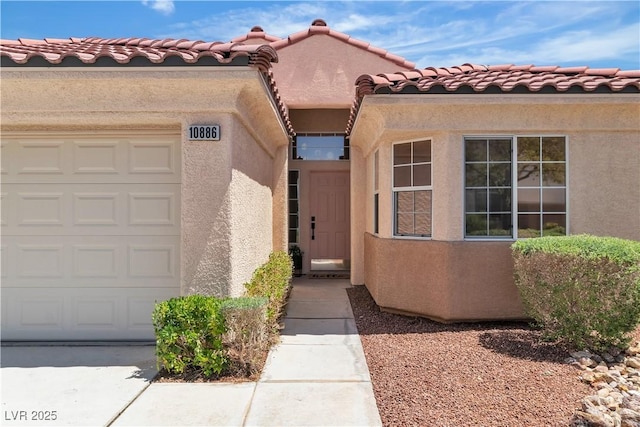 property entrance with a tiled roof, an attached garage, and stucco siding