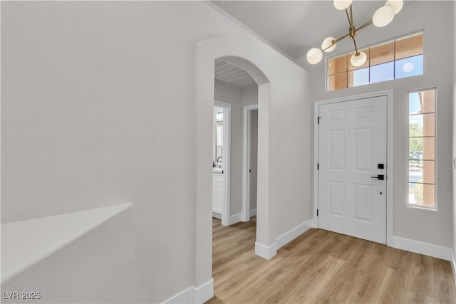 foyer entrance featuring arched walkways, baseboards, light wood-type flooring, and a chandelier