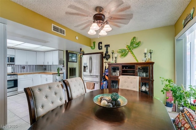 dining area featuring visible vents, a ceiling fan, a textured ceiling, and light tile patterned floors