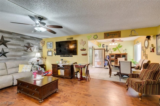 living room featuring a textured ceiling, ceiling fan, and visible vents