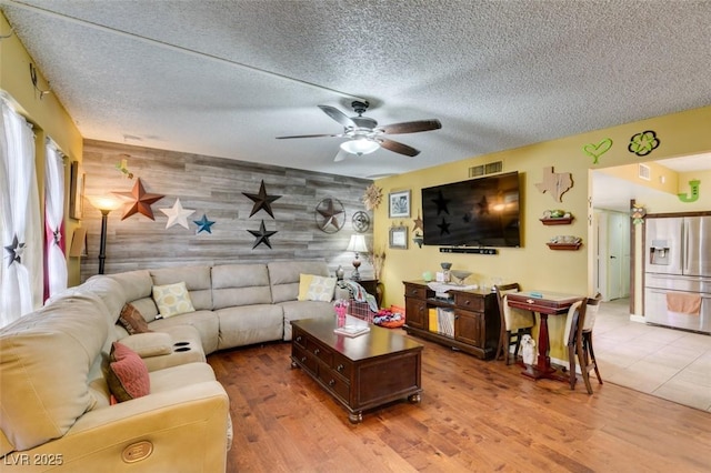 living room with a ceiling fan, visible vents, wood finished floors, and an accent wall