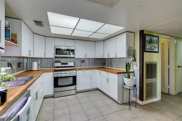 kitchen with a sink, appliances with stainless steel finishes, light tile patterned flooring, and wood counters
