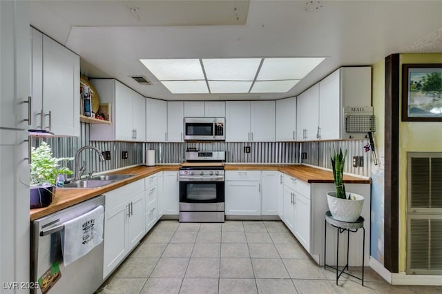 kitchen featuring butcher block countertops, a sink, appliances with stainless steel finishes, and light tile patterned floors