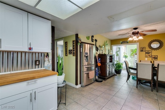 kitchen with baseboards, stainless steel fridge, white cabinetry, a ceiling fan, and light tile patterned floors