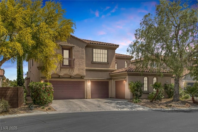 mediterranean / spanish-style house featuring an attached garage, stucco siding, driveway, and a tiled roof