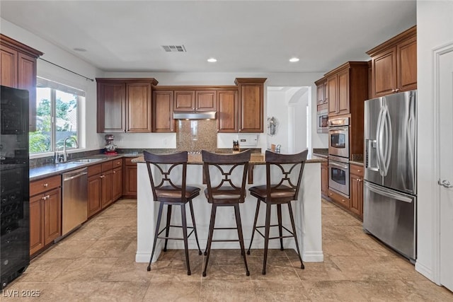 kitchen with dark countertops, a sink, stainless steel appliances, under cabinet range hood, and visible vents