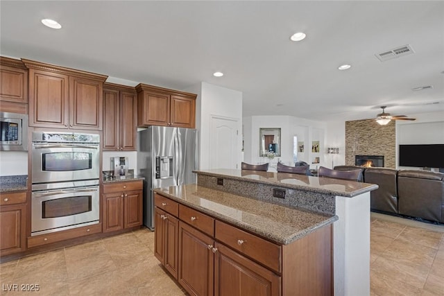 kitchen with ceiling fan, appliances with stainless steel finishes, brown cabinetry, a kitchen island, and visible vents