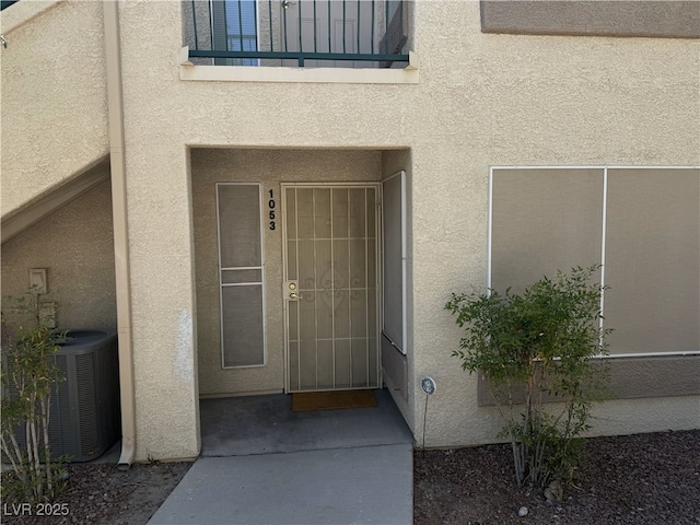 entrance to property featuring central air condition unit, stucco siding, and a balcony