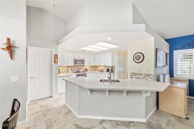5200 Wheatland Dr, Pahrump, NV 89061 - kitchen featuring light stone countertops, a sink, a peninsula, stainless steel microwave, and white cabinetry