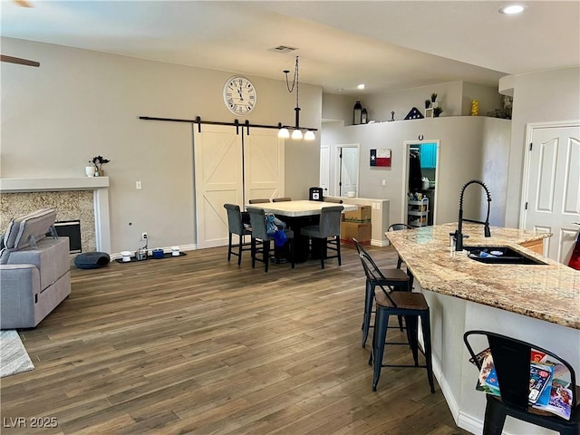 interior space with a sink, recessed lighting, wood finished floors, visible vents, and a center island with sink