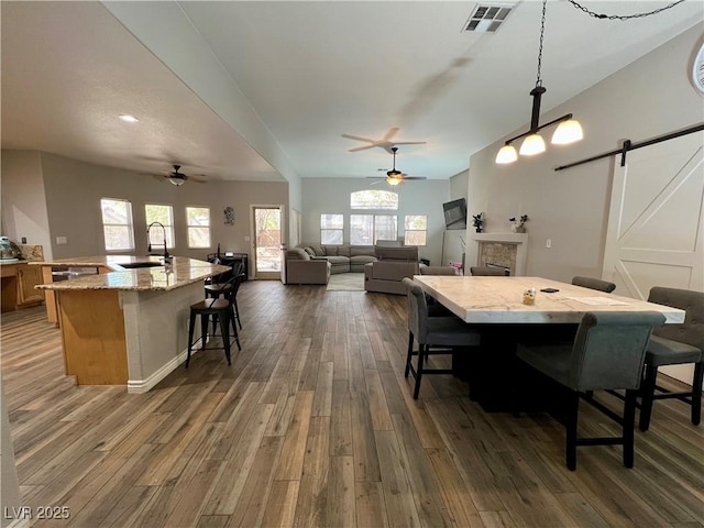 dining space with ceiling fan, visible vents, a barn door, and dark wood-type flooring