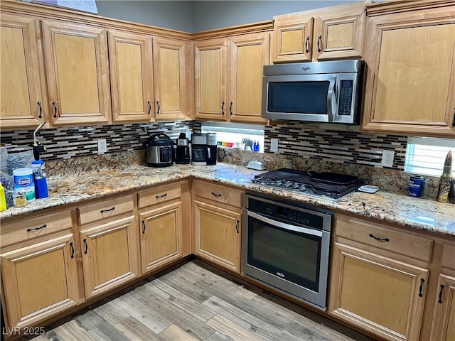 kitchen with appliances with stainless steel finishes, backsplash, light wood-type flooring, and light stone counters