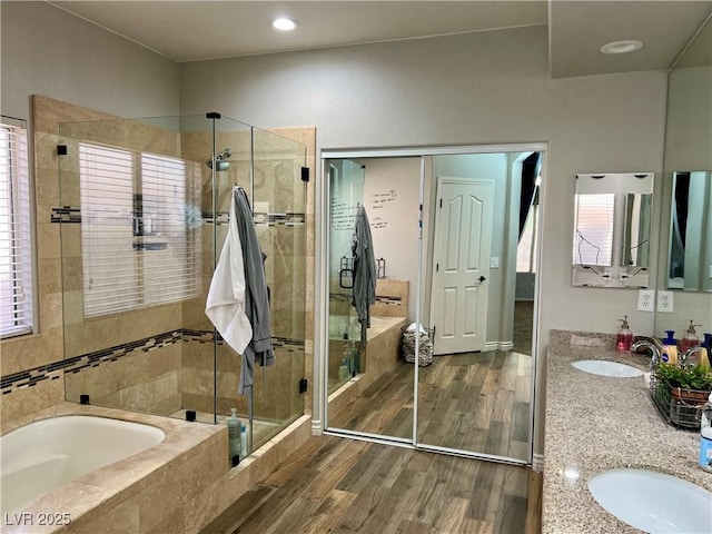 bathroom with a sink, double vanity, a shower stall, wood finished floors, and a bath