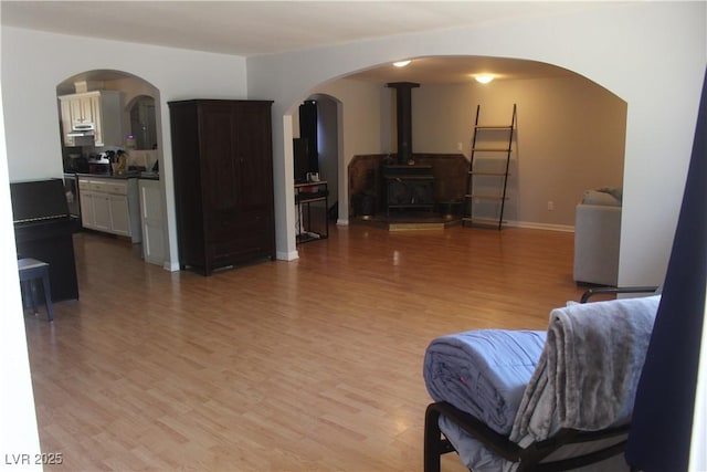 living area featuring light wood-type flooring, arched walkways, baseboards, and a wood stove
