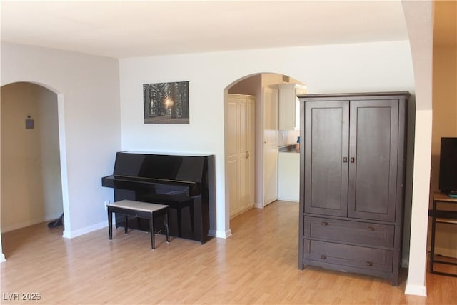 interior space with arched walkways, baseboards, and light wood-type flooring
