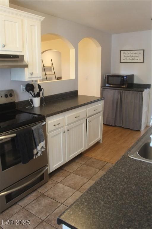 kitchen featuring dark countertops, appliances with stainless steel finishes, tile patterned flooring, white cabinetry, and under cabinet range hood