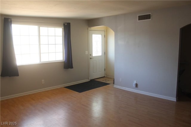 foyer with arched walkways, baseboards, visible vents, and wood finished floors