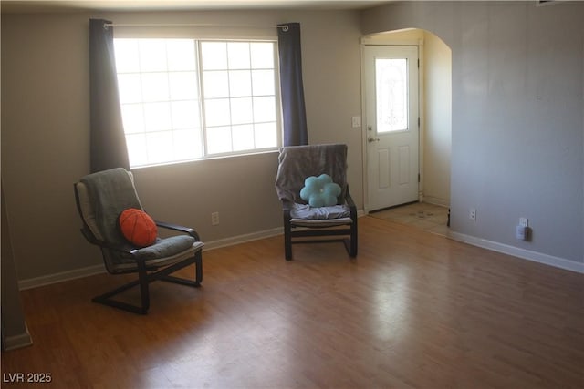 sitting room with baseboards, arched walkways, wood finished floors, and a wealth of natural light