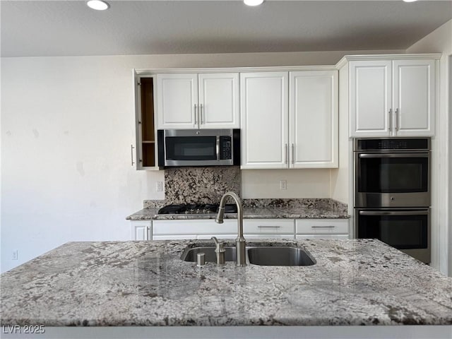 kitchen featuring recessed lighting, white cabinets, light stone counters, a sink, and appliances with stainless steel finishes