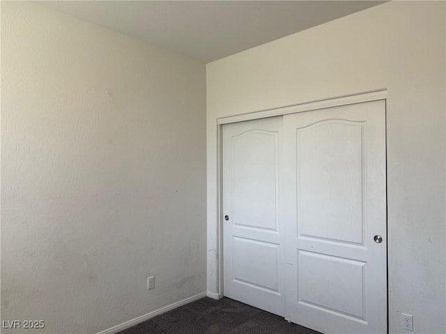 unfurnished bedroom featuring baseboards, a closet, and dark colored carpet