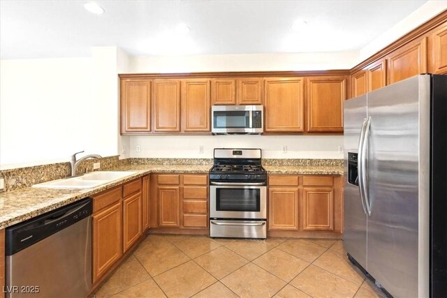 kitchen featuring brown cabinets, stainless steel appliances, light stone countertops, and a sink