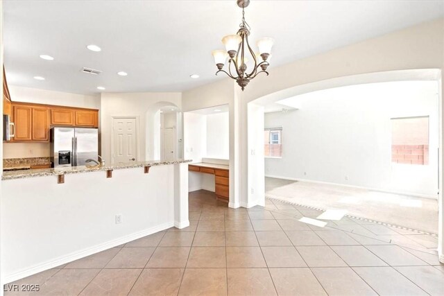 kitchen featuring a kitchen breakfast bar, brown cabinetry, appliances with stainless steel finishes, arched walkways, and a notable chandelier