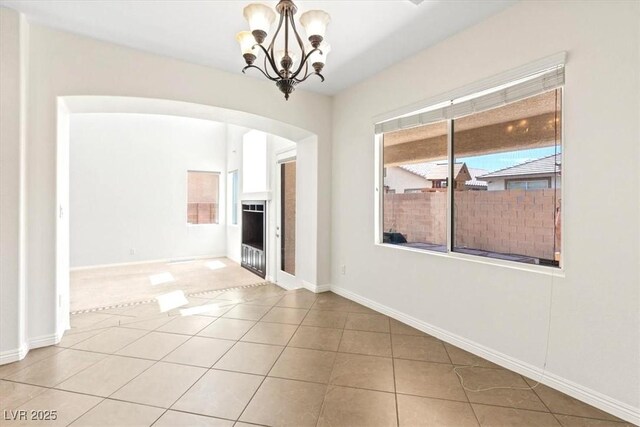 unfurnished room featuring arched walkways, tile patterned floors, a notable chandelier, and baseboards