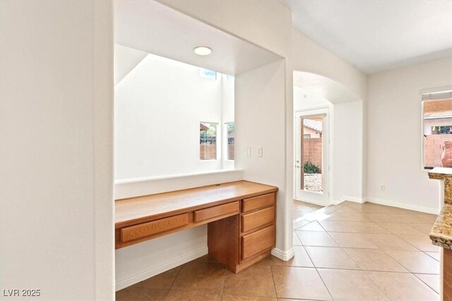 hallway with baseboards, arched walkways, and light tile patterned floors