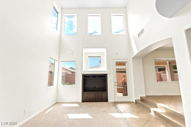 unfurnished living room featuring a healthy amount of sunlight, arched walkways, tile patterned flooring, and a towering ceiling