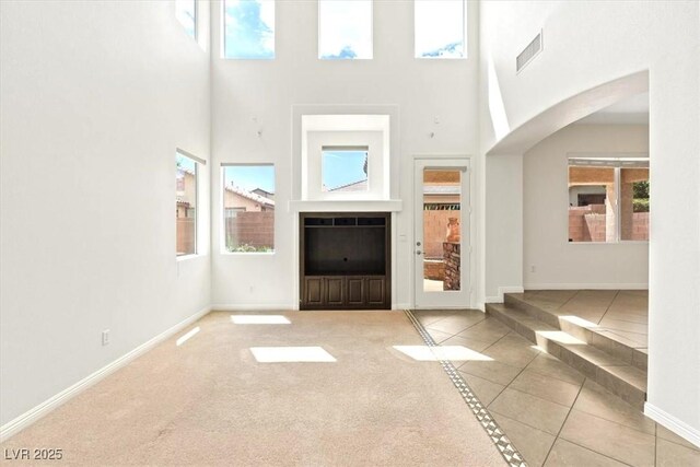 unfurnished living room with visible vents, arched walkways, tile patterned flooring, baseboards, and a high ceiling