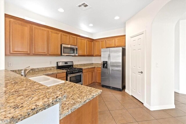 kitchen with brown cabinets, a sink, arched walkways, stainless steel appliances, and light tile patterned floors