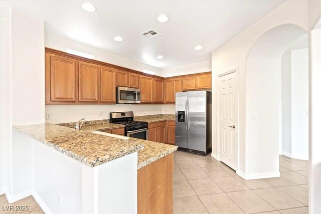 kitchen with appliances with stainless steel finishes, light tile patterned floors, brown cabinets, and light stone countertops