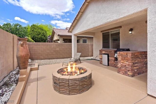 view of patio / terrace featuring a fenced backyard, a fire pit, area for grilling, and an outdoor kitchen