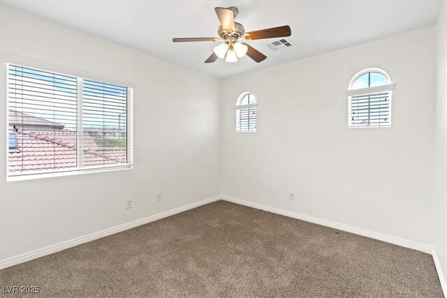 spare room with baseboards, visible vents, dark colored carpet, and a wealth of natural light