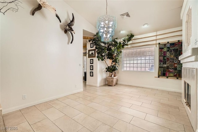 unfurnished living room featuring a glass covered fireplace, baseboards, visible vents, and a chandelier