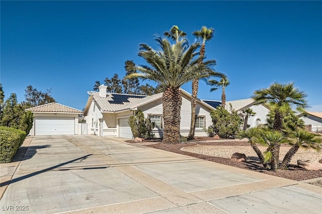 view of front of property with a tiled roof, a chimney, a detached garage, roof mounted solar panels, and stucco siding