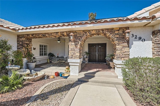 entrance to property featuring a patio area, stucco siding, a tile roof, and stone siding