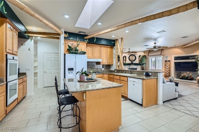 kitchen featuring a peninsula, white appliances, open floor plan, a kitchen breakfast bar, and a sink