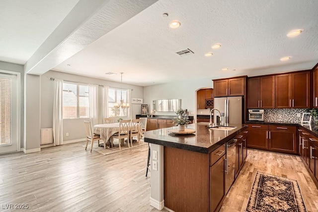 kitchen with a kitchen island with sink, visible vents, a sink, stainless steel fridge with ice dispenser, and light wood-style flooring
