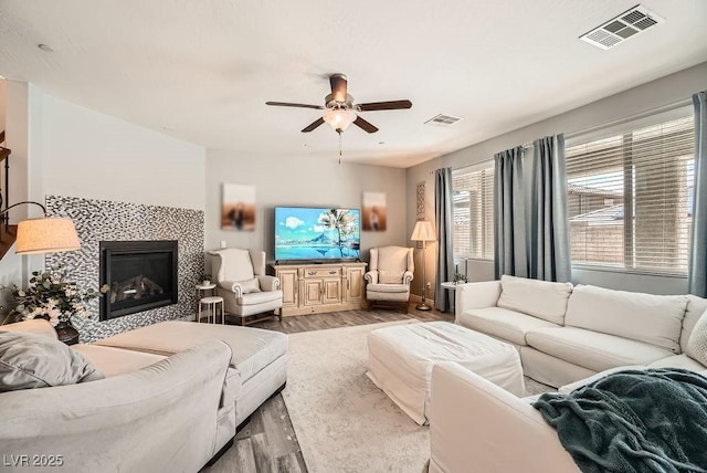 living area with visible vents, ceiling fan, wood finished floors, and a tile fireplace