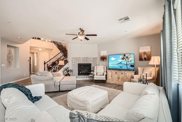 living room featuring ceiling fan, stairs, baseboards, wood finished floors, and visible vents
