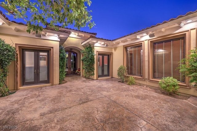 view of exterior entry with a patio area, stucco siding, and french doors