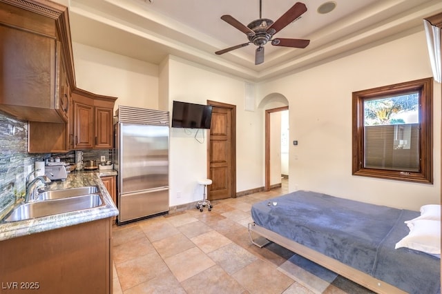 bedroom with a sink, a raised ceiling, arched walkways, and built in fridge