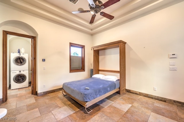 bedroom featuring stacked washing maching and dryer, stone tile floors, a ceiling fan, baseboards, and visible vents