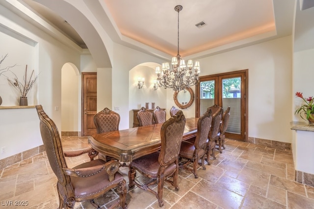 dining area with arched walkways, a chandelier, a tray ceiling, visible vents, and stone tile flooring